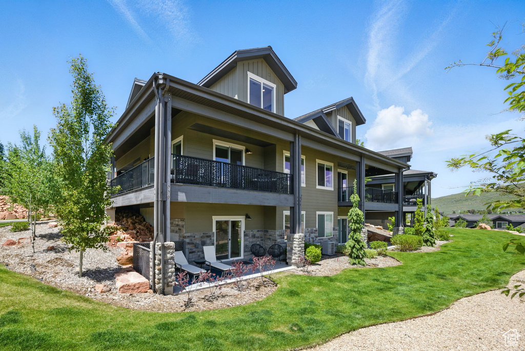 Rear view of house featuring a balcony, central AC, a yard, and stone siding