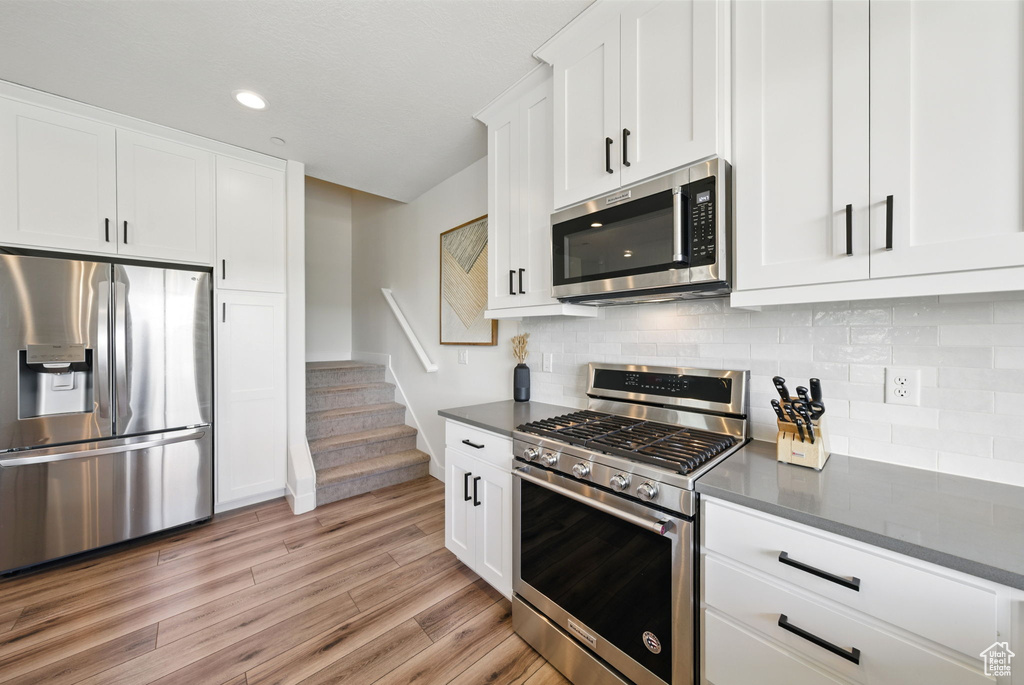 Kitchen featuring stainless steel appliances, dark countertops, light wood finished floors, white cabinetry, and recessed lighting