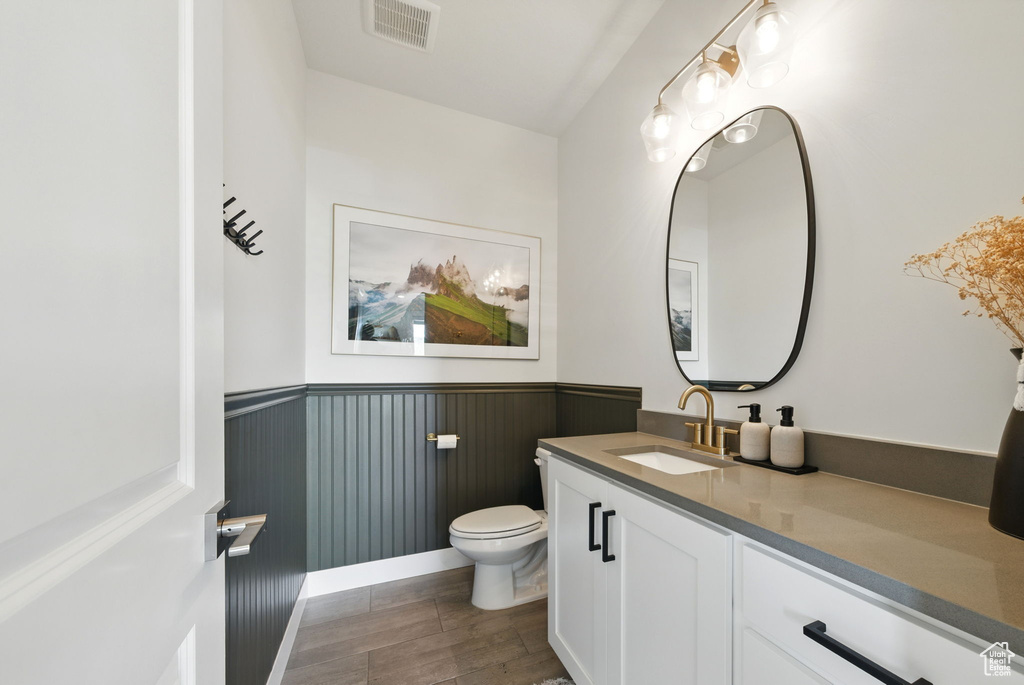 Bathroom featuring toilet, a wainscoted wall, vanity, and wood finished floors