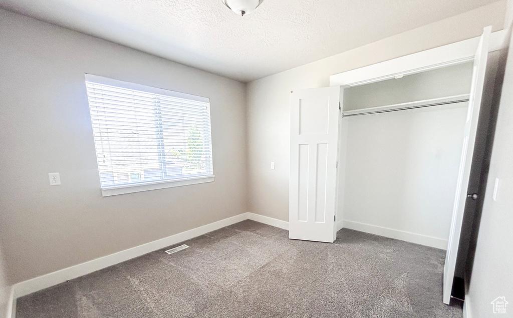 Unfurnished bedroom with carpet floors, a textured ceiling, a closet, and baseboards