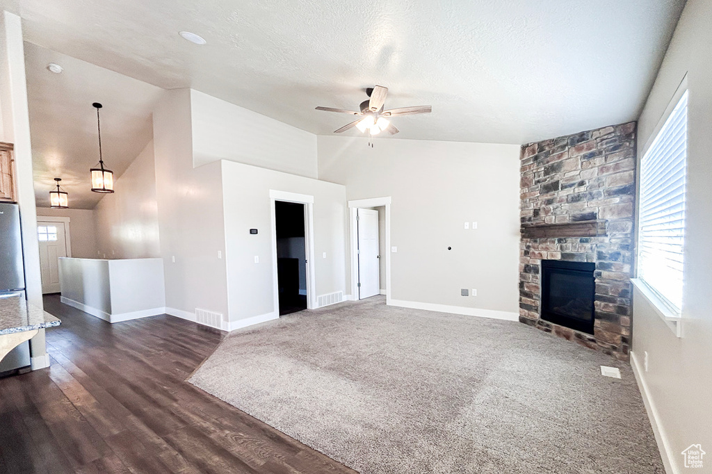 Unfurnished living room featuring a ceiling fan, vaulted ceiling, baseboards, a fireplace, and dark wood-type flooring