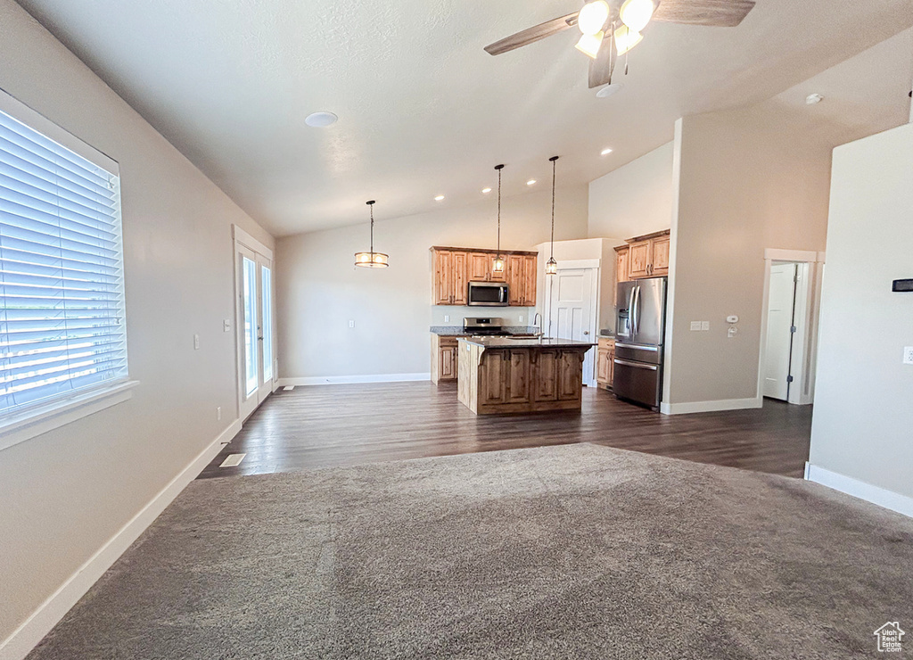Kitchen with stainless steel appliances, open floor plan, vaulted ceiling, dark colored carpet, and an island with sink