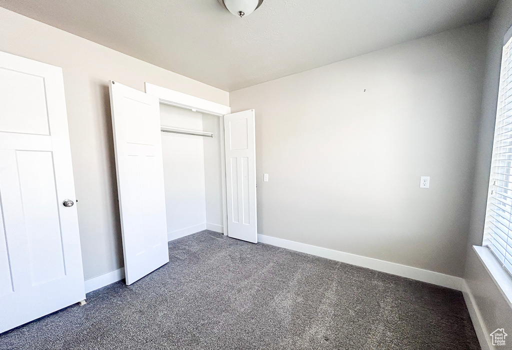 Unfurnished bedroom featuring dark carpet, baseboards, and a closet