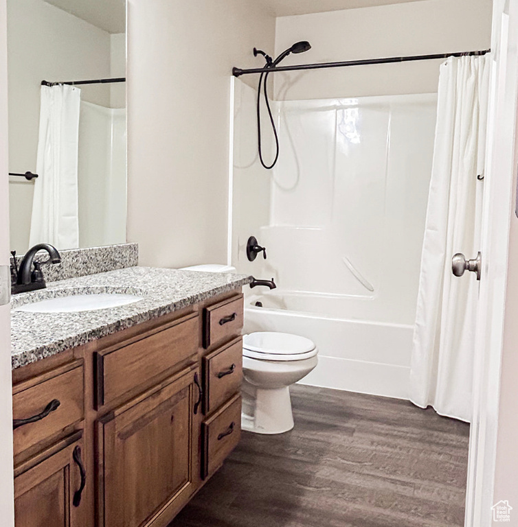 Bathroom with toilet, vanity, shower / bathtub combination with curtain, and wood finished floors