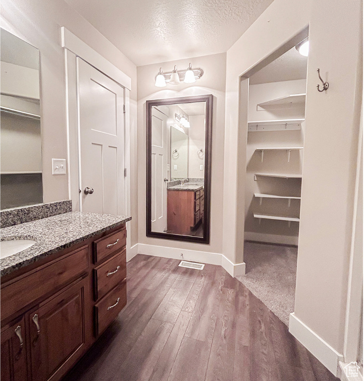 Bathroom with a walk in closet, wood finished floors, vanity, and a textured ceiling