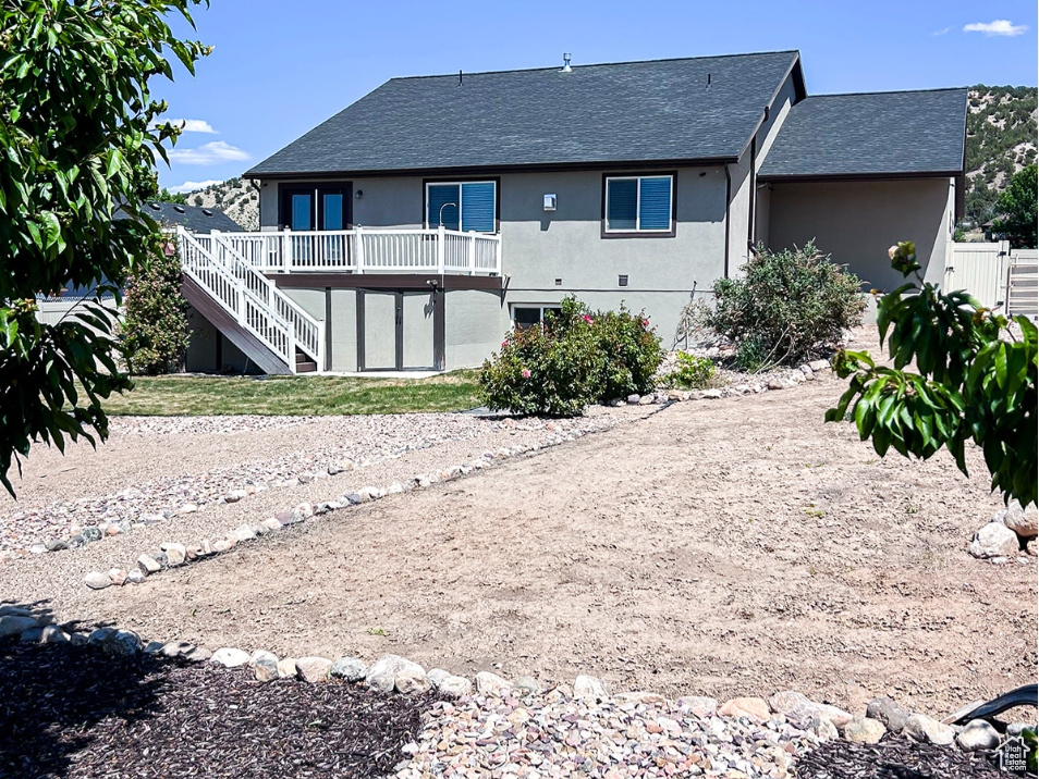 Rear view of house featuring stairs, stucco siding, roof with shingles, and a wooden deck