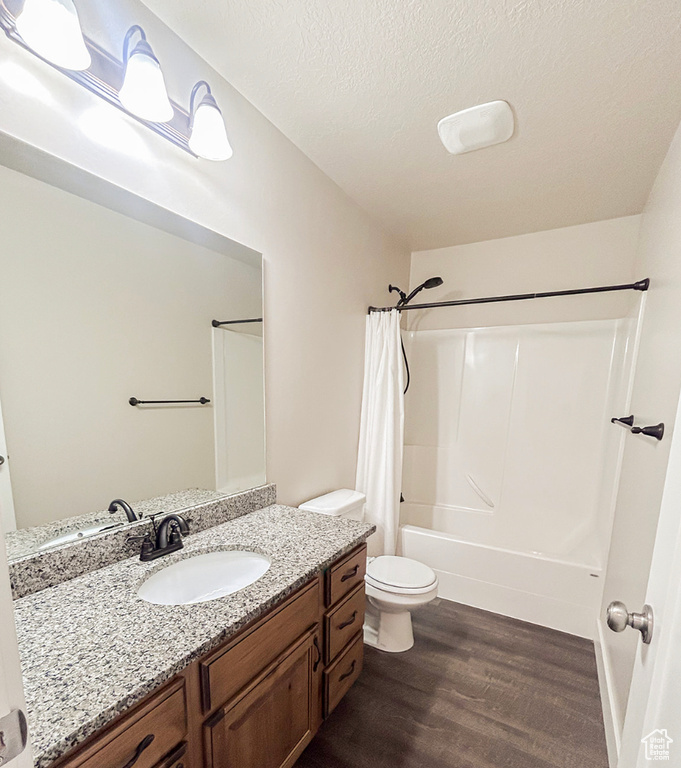 Full bathroom with wood finished floors, vanity, shower / bathtub combination with curtain, toilet, and a textured ceiling