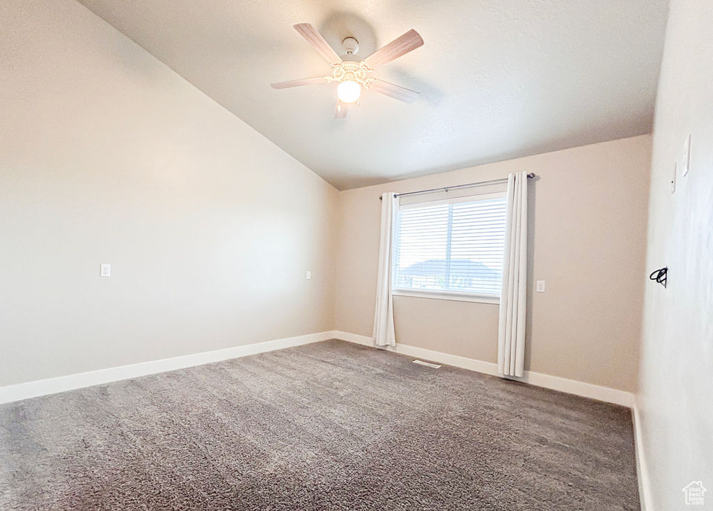 Carpeted empty room featuring lofted ceiling, a ceiling fan, and baseboards