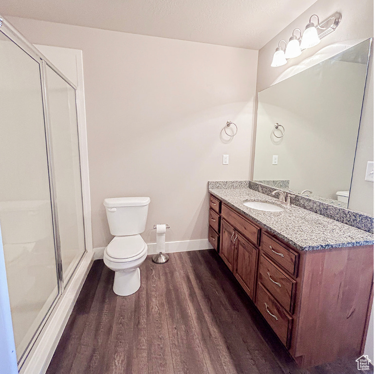 Bathroom with toilet, wood finished floors, vanity, a stall shower, and baseboards