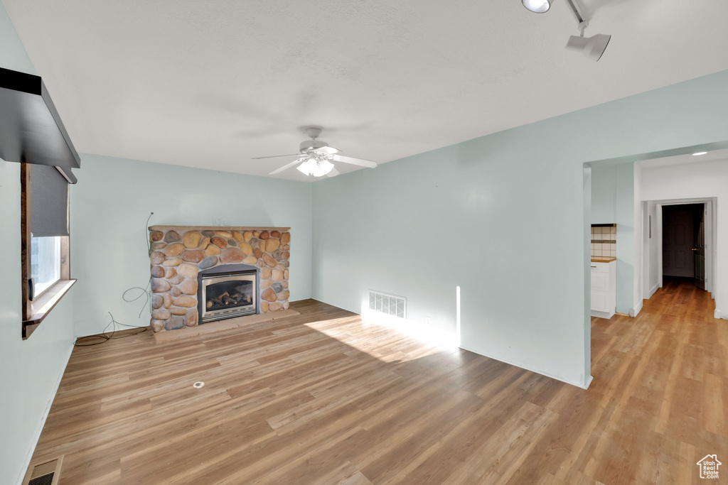 Unfurnished living room with ceiling fan, light wood-style floors, and a fireplace