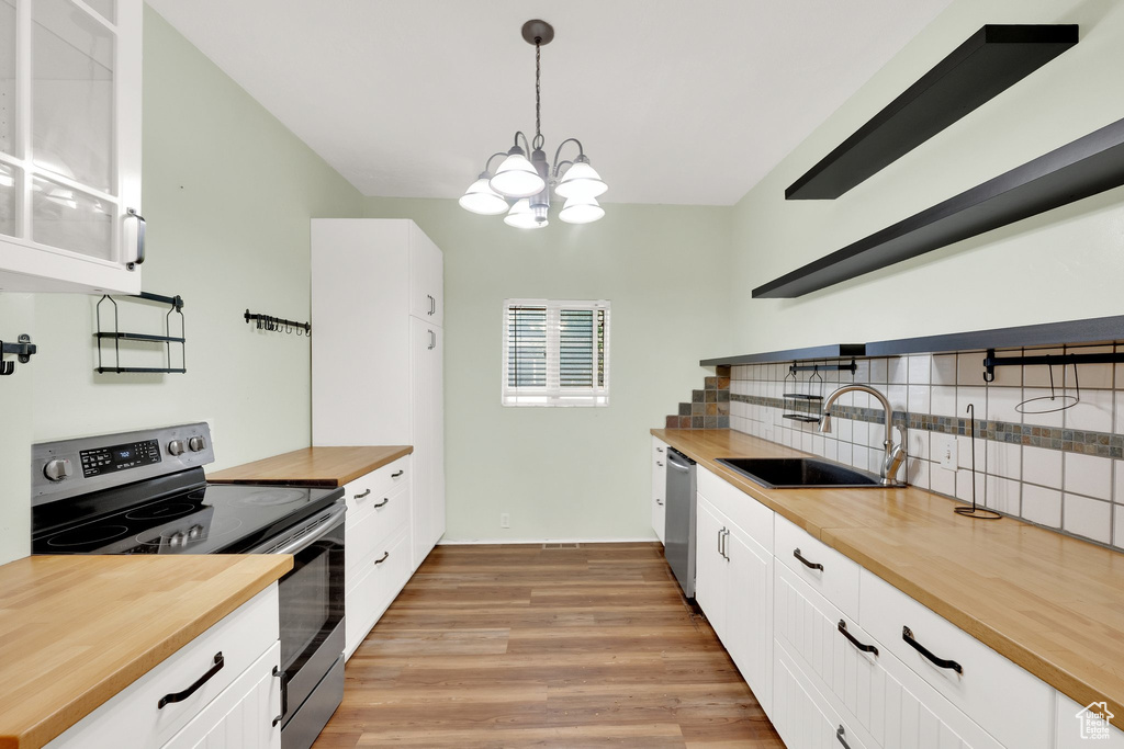 Kitchen with butcher block countertops, appliances with stainless steel finishes, open shelves, a sink, and tasteful backsplash