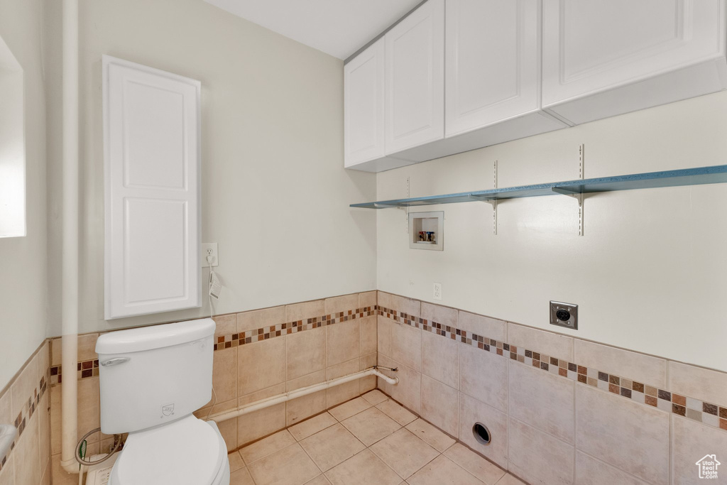 Laundry room featuring electric dryer hookup, tile walls, washer hookup, a wainscoted wall, and light tile patterned floors