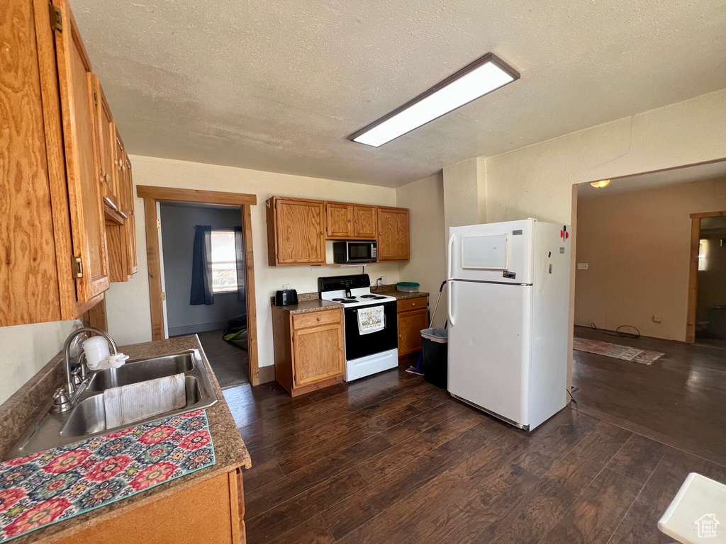 Kitchen with white appliances, a sink, dark wood-style floors, brown cabinets, and a textured ceiling