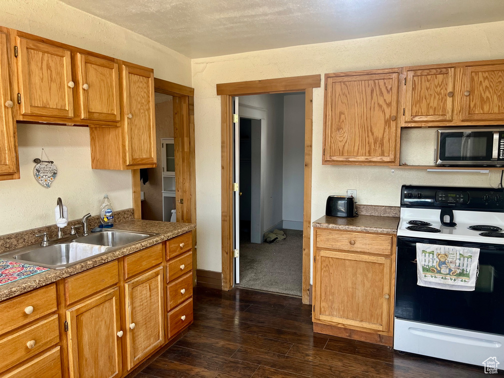 Kitchen featuring electric range oven, stainless steel microwave, a sink, dark wood finished floors, and brown cabinetry