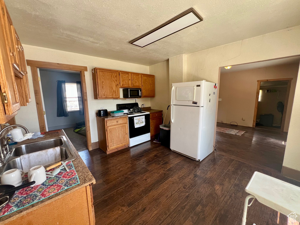 Kitchen with white appliances, a sink, dark wood-style floors, a textured ceiling, and brown cabinets