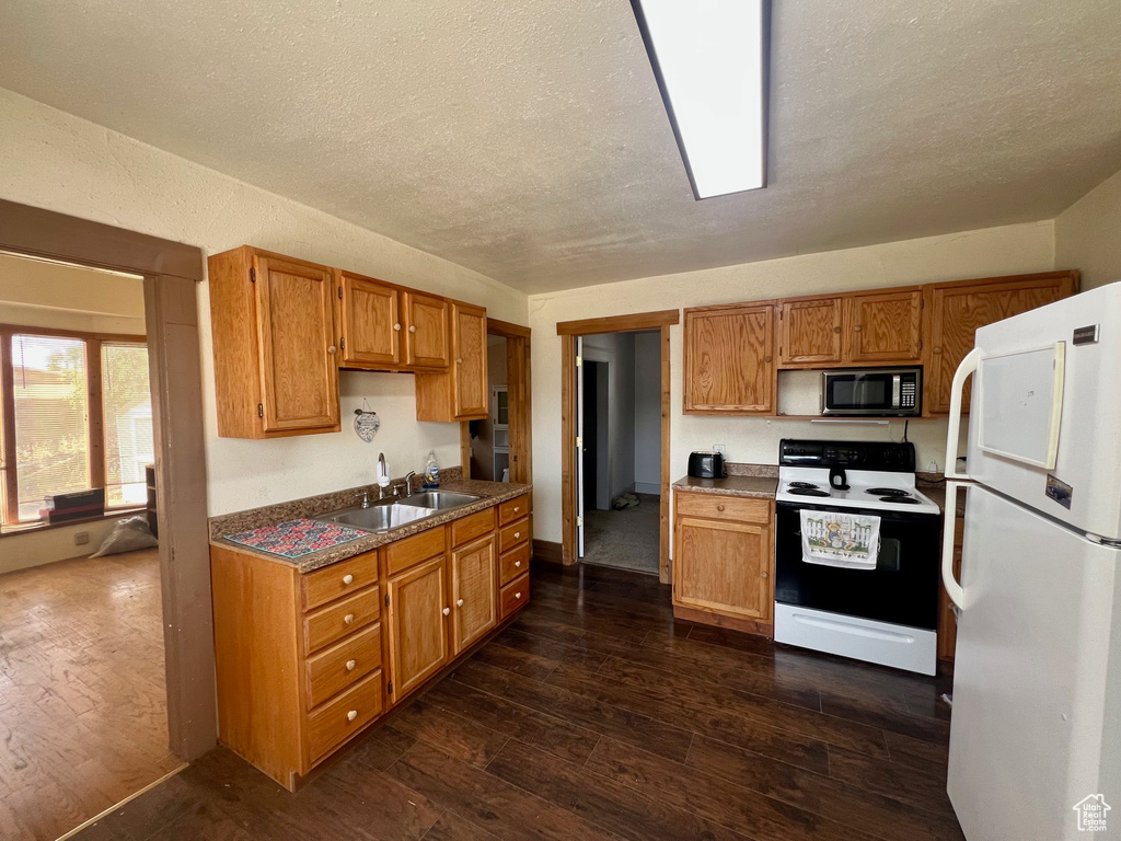 Kitchen with freestanding refrigerator, electric stove, stainless steel microwave, a sink, and dark wood-type flooring