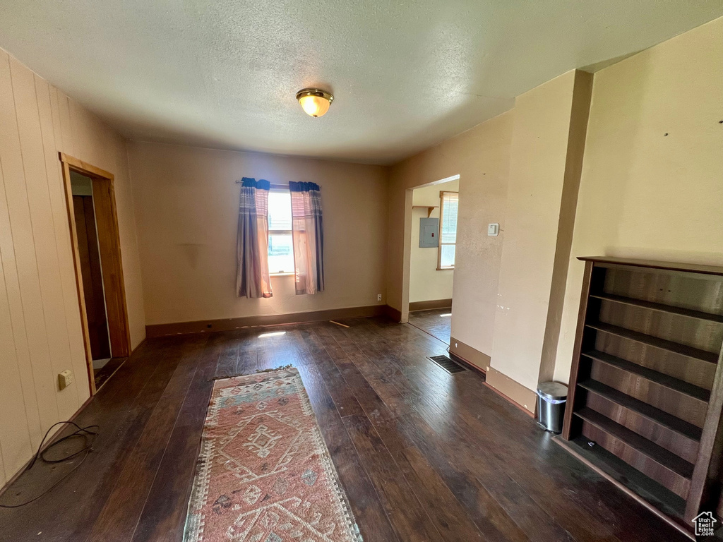 Empty room featuring dark wood-style flooring, a textured ceiling, electric panel, and baseboards