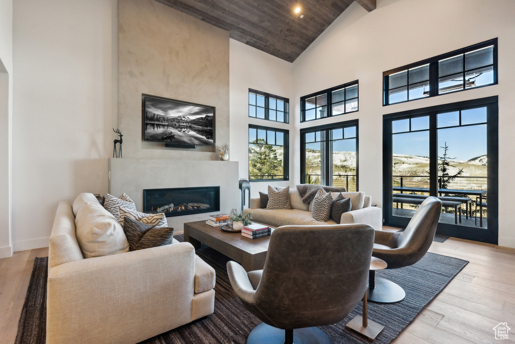 Living room with high vaulted ceiling, a high end fireplace, wooden ceiling, wood finished floors, and baseboards
