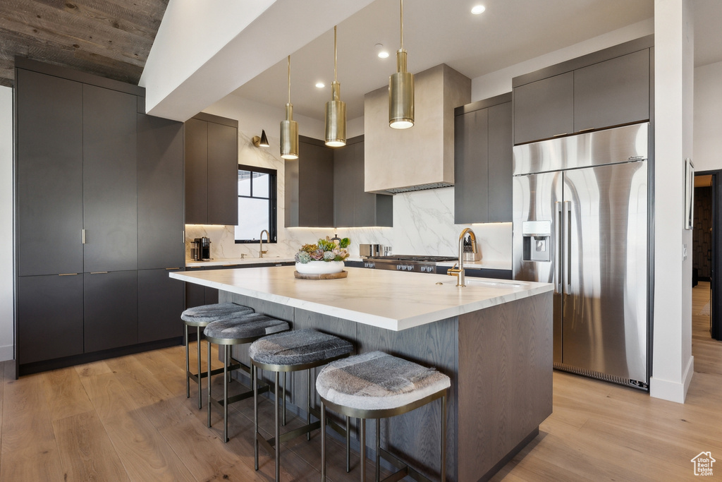 Kitchen featuring stainless steel fridge with ice dispenser, modern cabinets, a sink, an island with sink, and recessed lighting