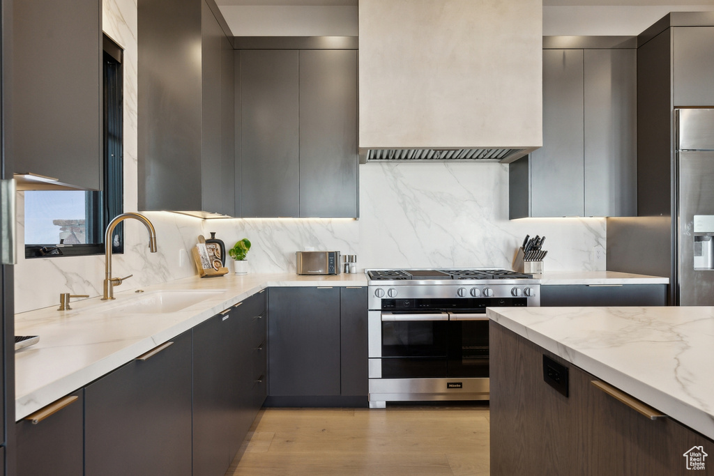 Kitchen with appliances with stainless steel finishes, a sink, light stone counters, modern cabinets, and gray cabinetry