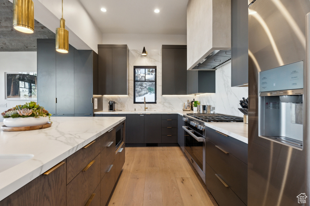 Kitchen with stainless steel appliances, modern cabinets, premium range hood, light wood-style flooring, and a sink