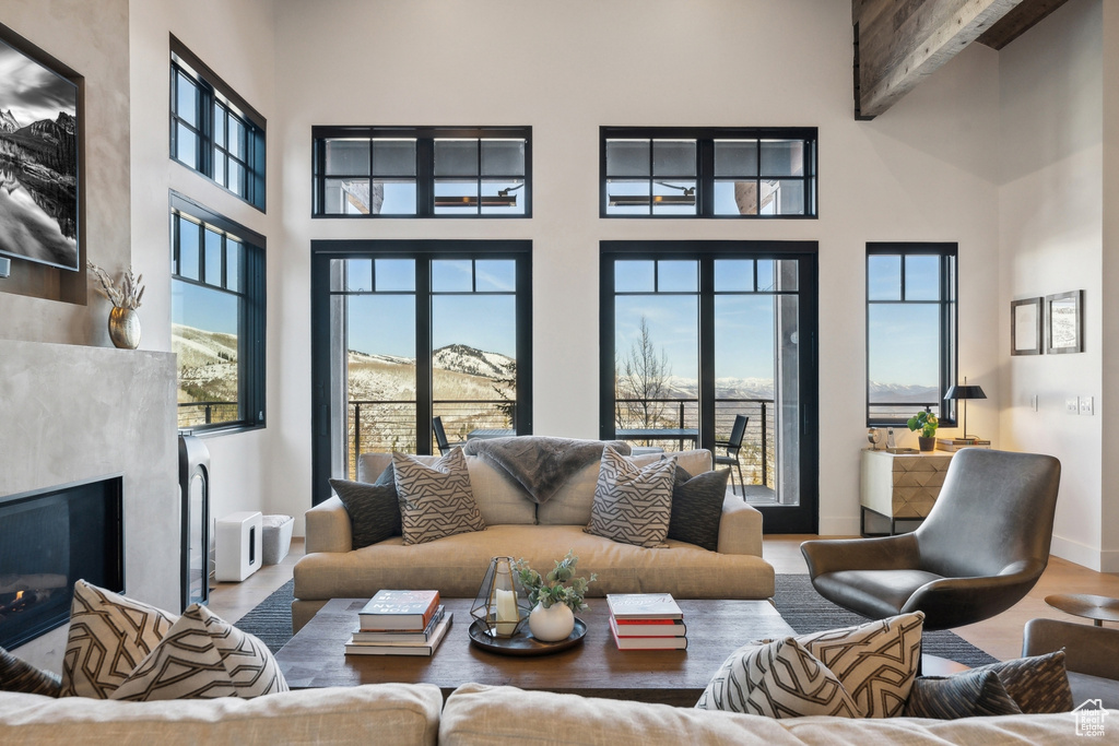 Living room featuring a high ceiling, a fireplace, beamed ceiling, and wood finished floors