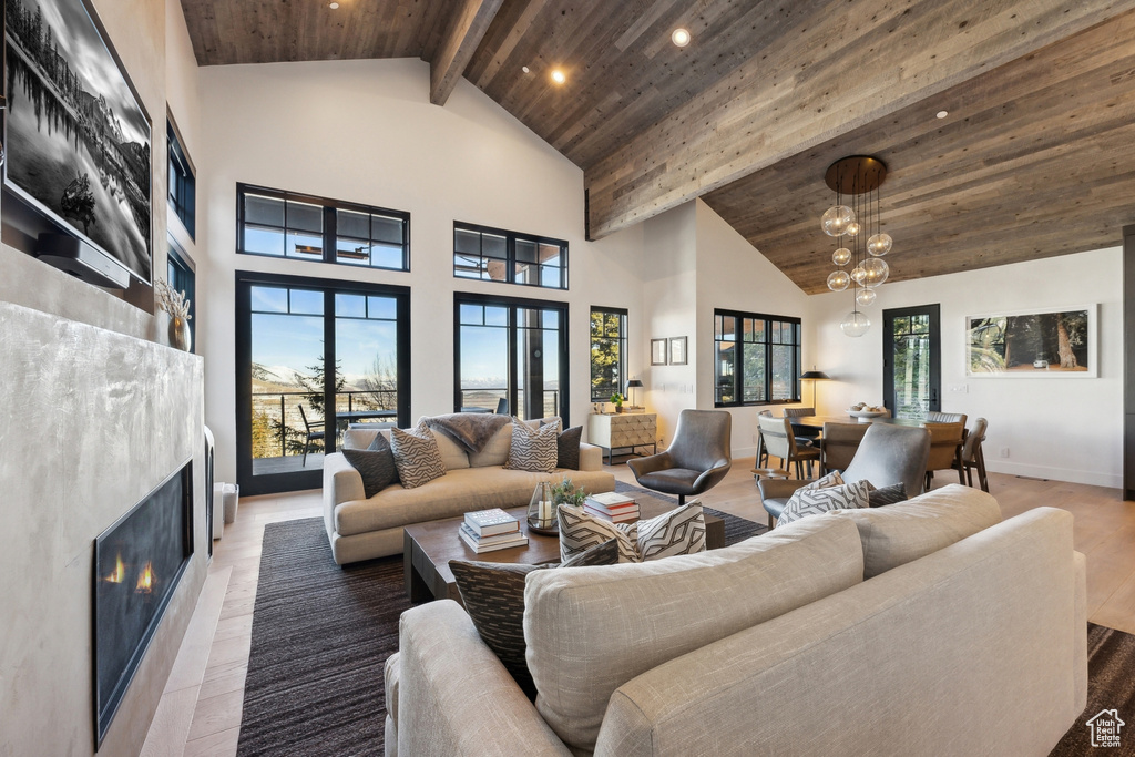 Living room with wooden ceiling with exposed beams, a lit fireplace, high vaulted ceiling, recessed lighting, and a chandelier