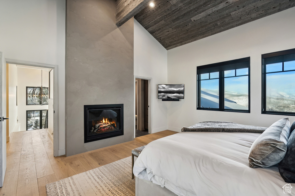 Bedroom featuring high vaulted ceiling, a large fireplace, light wood finished floors, baseboards, and wood ceiling