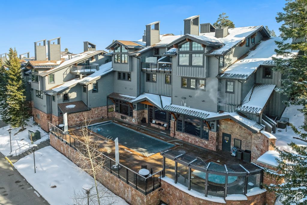 Snow covered back of property with board and batten siding, a chimney, stone siding, and a residential view