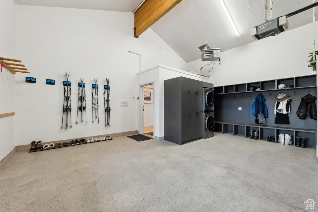 Garage with stacked washer and clothes dryer, a garage door opener, a heating unit, and baseboards