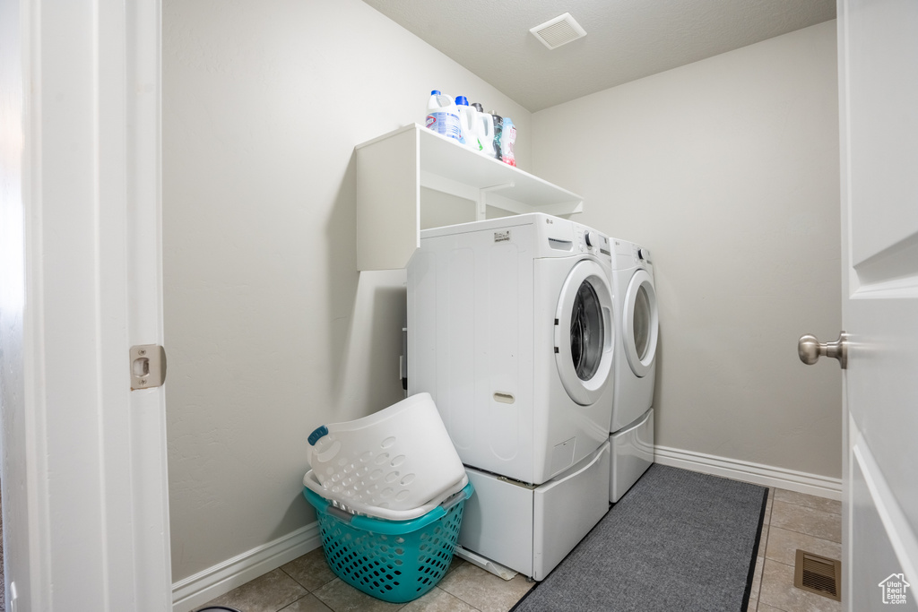 Laundry area with washing machine and clothes dryer, light tile patterned floors, and baseboards
