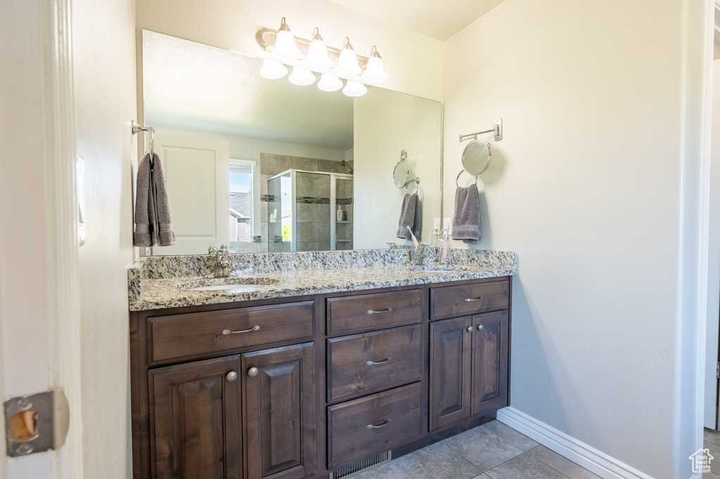 Bathroom with double vanity, a shower stall, tile patterned flooring, and baseboards