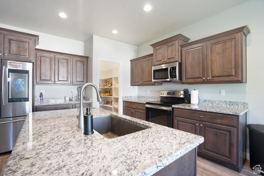 Kitchen with appliances with stainless steel finishes, light wood-style flooring, light stone countertops, a sink, and recessed lighting