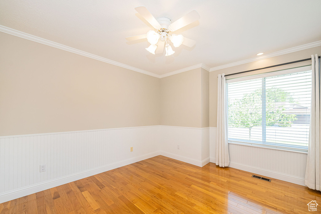 Empty room featuring light wood finished floors, baseboards, wainscoting, ornamental molding, and a ceiling fan