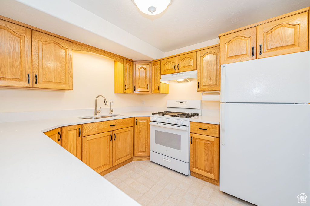 Kitchen with white appliances, a sink, under cabinet range hood, light countertops, and light flooring