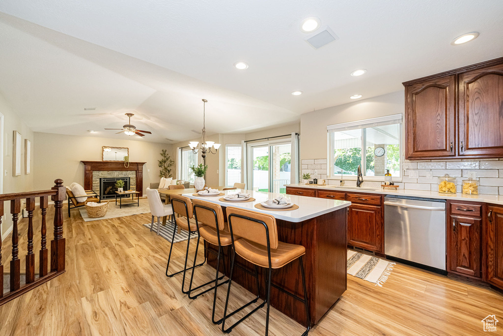 Kitchen with stainless steel dishwasher, a kitchen bar, light wood-type flooring, a fireplace, and recessed lighting