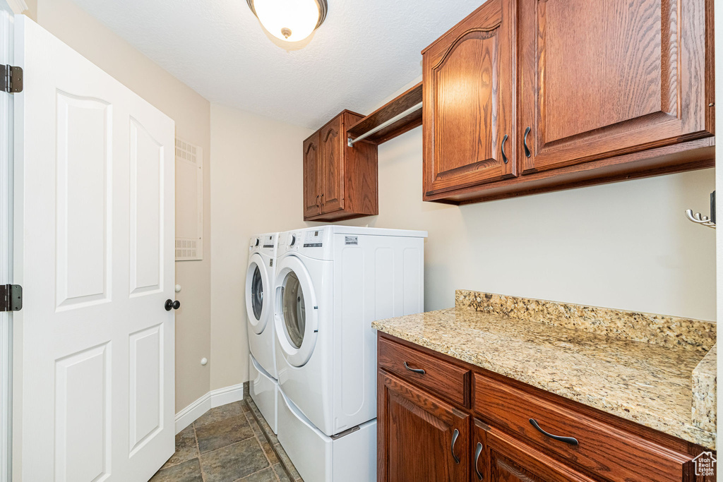 Laundry area with washing machine and clothes dryer, cabinet space, baseboards, and dark stone finish flooring