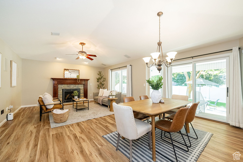 Dining room featuring light wood finished floors, a stone fireplace, a chandelier, and baseboards