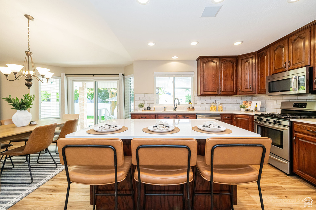 Kitchen with stainless steel appliances, light countertops, a kitchen island, decorative backsplash, and a kitchen bar