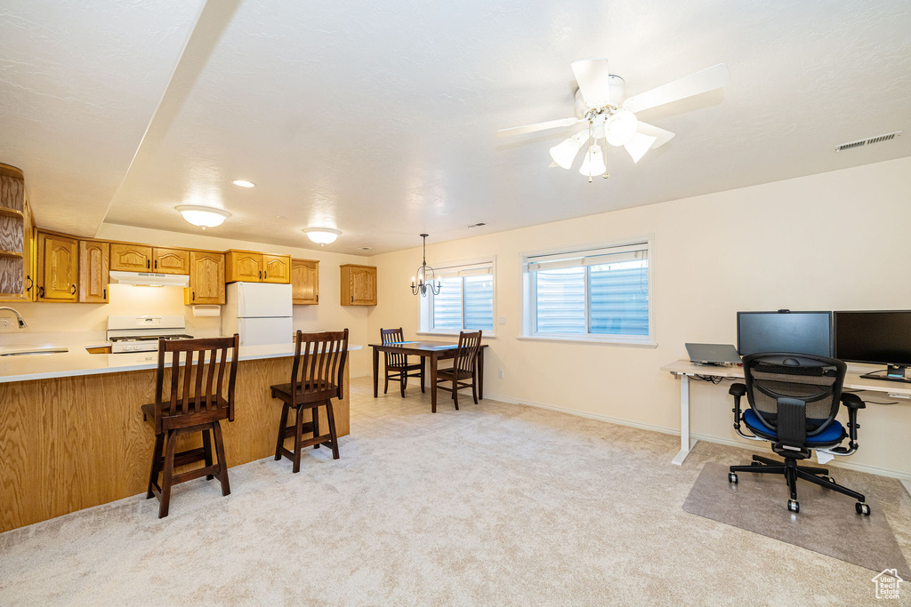 Kitchen featuring white appliances, under cabinet range hood, a sink, a peninsula, and light countertops