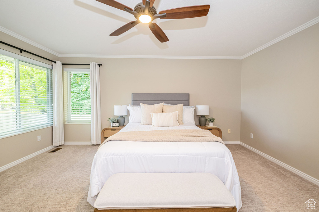 Bedroom with light colored carpet, ornamental molding, baseboards, and ceiling fan