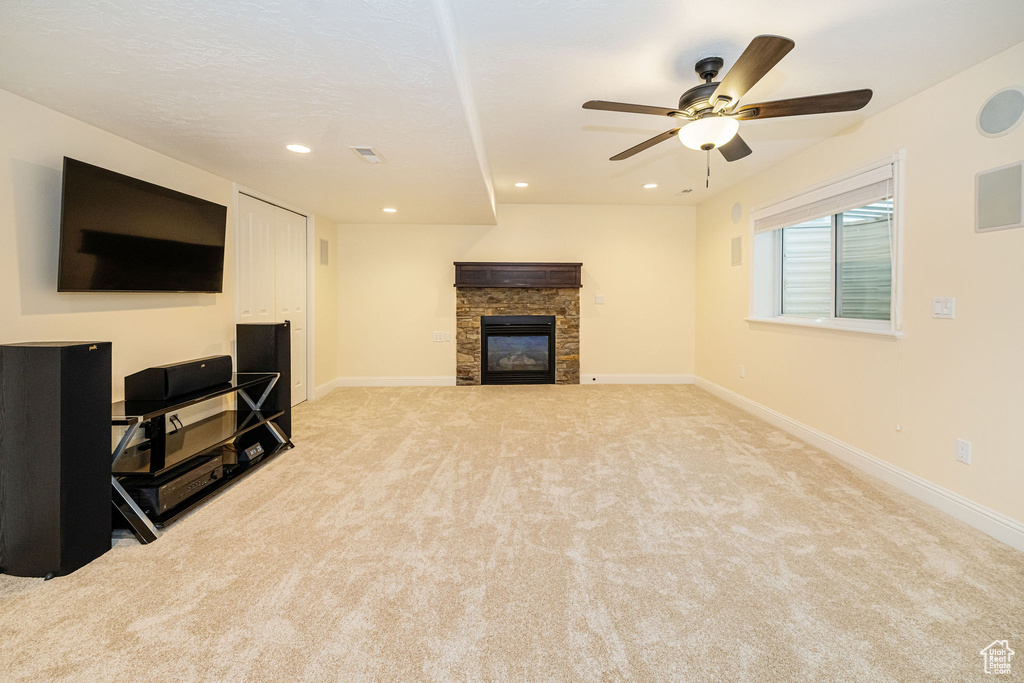 Unfurnished living room with light colored carpet, a ceiling fan, a stone fireplace, baseboards, and recessed lighting