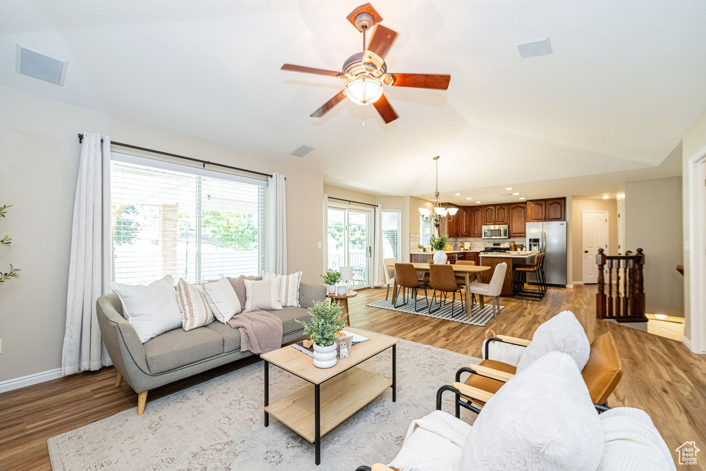 Living area with lofted ceiling, light wood-style floors, a chandelier, baseboards, and a ceiling fan