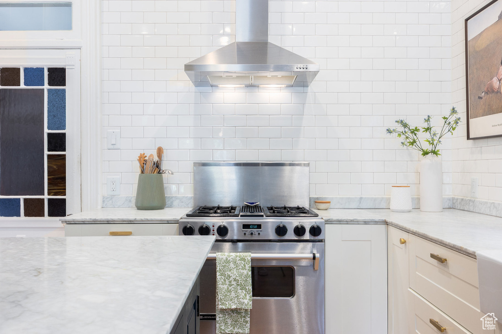 Kitchen featuring wall chimney exhaust hood, stainless steel gas range, and tasteful backsplash