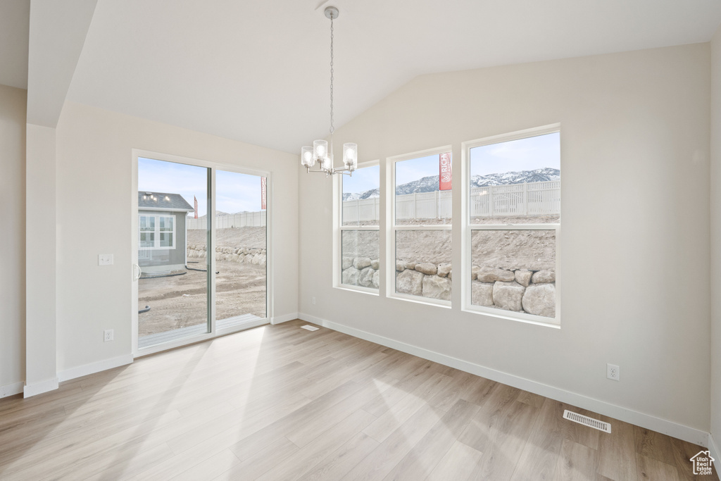 Unfurnished dining area featuring a chandelier, light wood-style flooring, vaulted ceiling, and baseboards