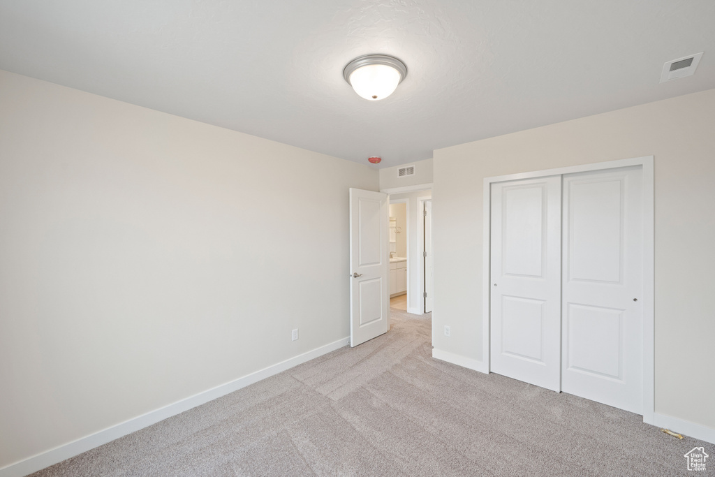 Unfurnished bedroom featuring light colored carpet, baseboards, and a closet