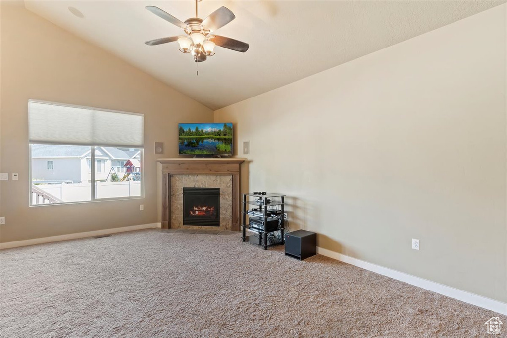 Carpeted living room with ceiling fan, a tile fireplace, lofted ceiling, and baseboards