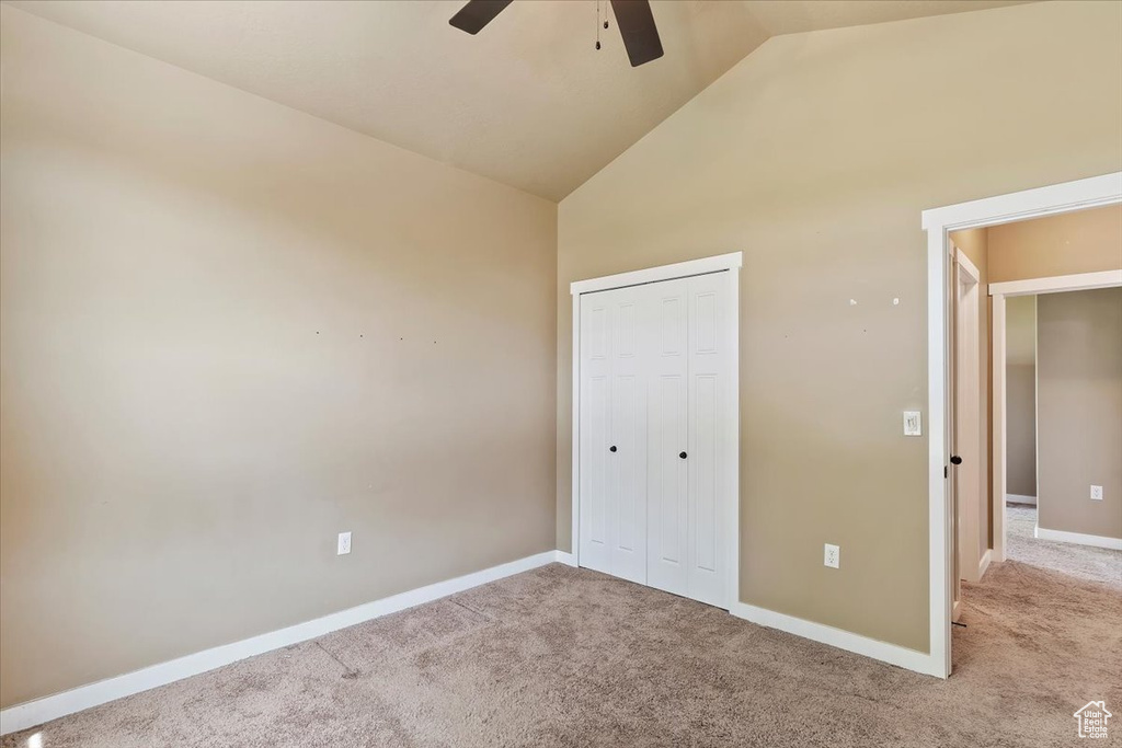 Unfurnished bedroom featuring carpet, high vaulted ceiling, a closet, baseboards, and a ceiling fan