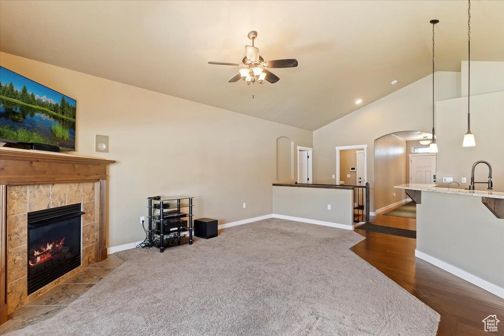 Living room featuring ceiling fan, arched walkways, high vaulted ceiling, a fireplace, and dark colored carpet