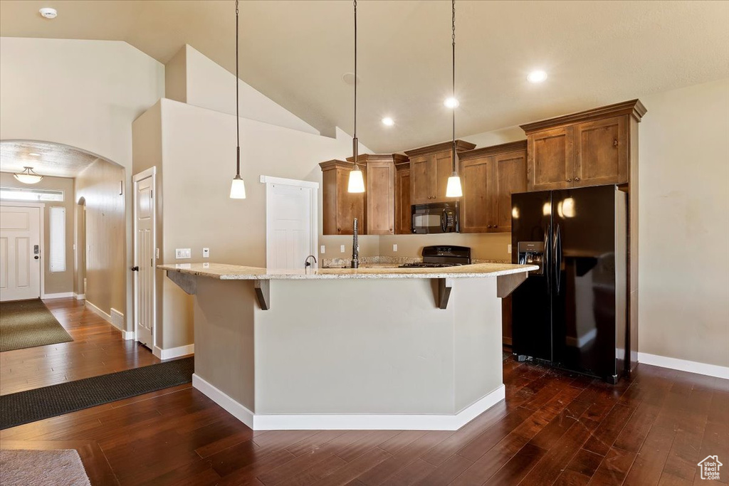 Kitchen with black appliances, brown cabinetry, a kitchen breakfast bar, dark wood finished floors, and arched walkways